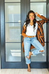 a woman in jeans and a Zilker Belts ATX Light cardigan standing in front of a door.