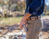 Man wearing a light brown leather belt with black and white stitching. He holds a beer in one hand.